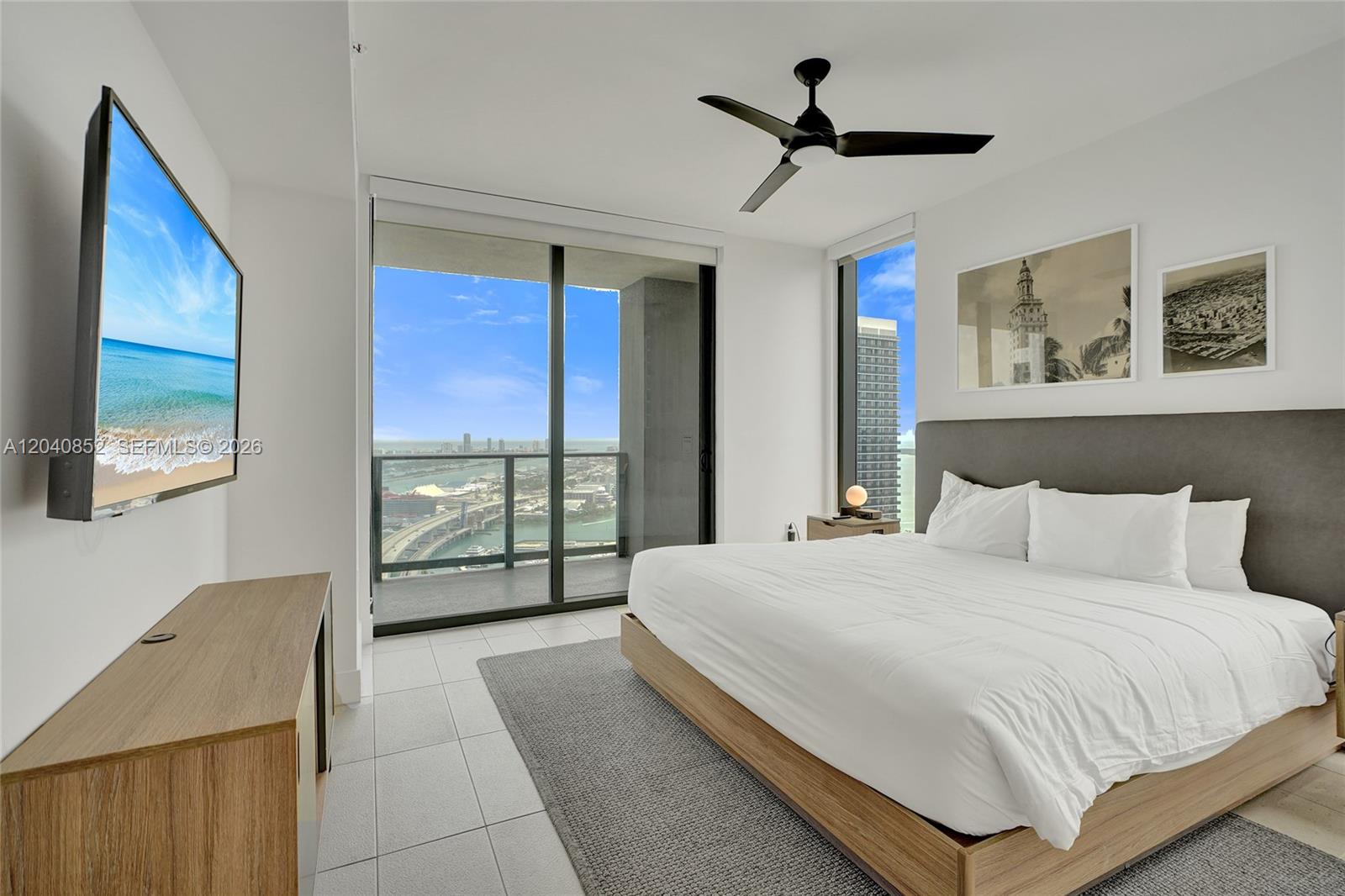 A modern bedroom features a king bed, wall-mounted television, and floor-to-ceiling windows with city views — 159 NE 6th St # 3916, Miami FL 33132, MIAMI, FL
