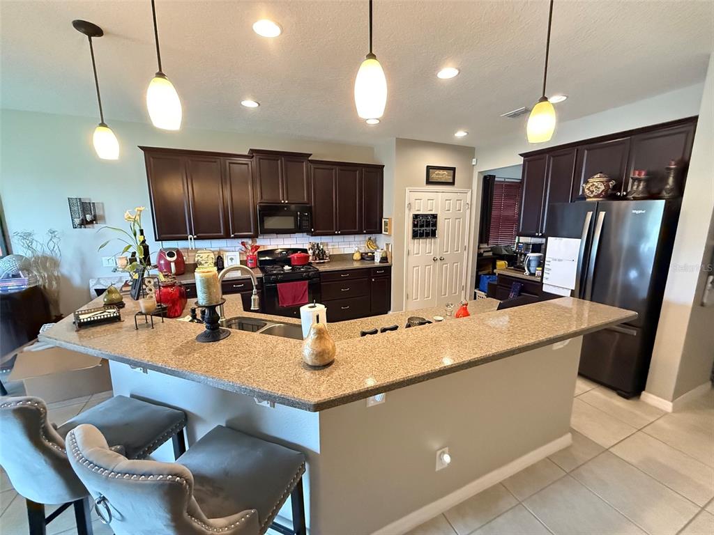 A kitchen features dark wood cabinets, granite countertops, a breakfast bar, and stainless steel appliances — 2228 NAPONE LANE, MINNEOLA, FL