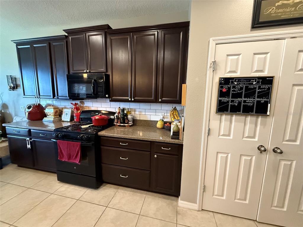 A kitchen features dark wood cabinets, a black stove, and a white subway tile backsplash — 2228 NAPONE LANE, MINNEOLA, FL