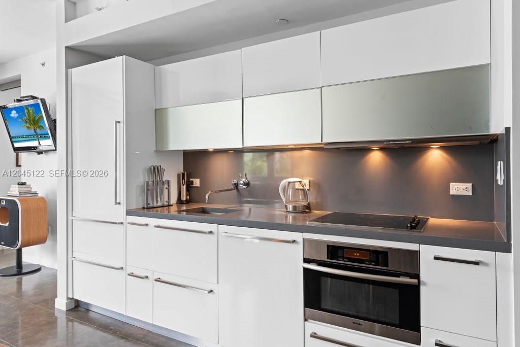 A modern kitchen features white cabinetry, a dark gray countertop, and stainless steel appliances — 220 21st St # 401, Miami Beach FL 33139, MIAMI BEACH, FL