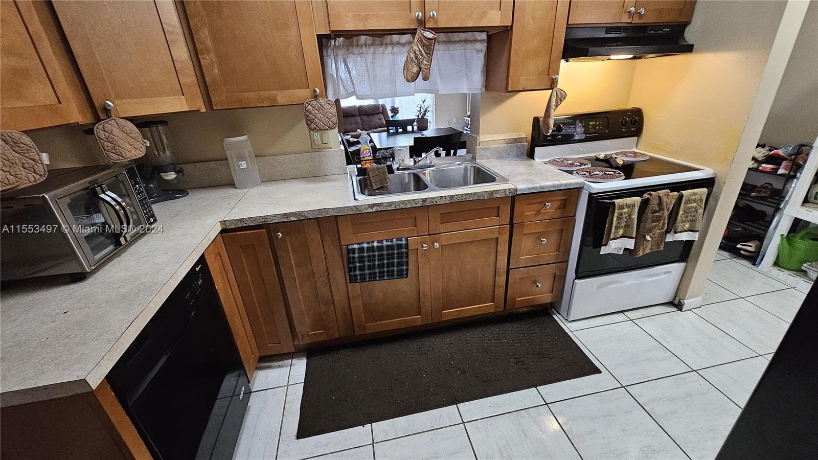A kitchen features wood cabinets, a double sink, a black stove, and white tile flooring — 2800 NW 56th Ave # A403, Lauderhill FL 33313, LAUDERHILL, FL