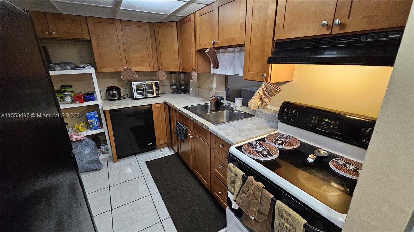 A kitchen features wood cabinets, a black dishwasher, a black stove, and white tile flooring — 2800 NW 56th Ave # A403, Lauderhill FL 33313, LAUDERHILL, FL