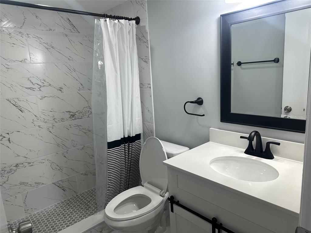 A bathroom features a marble-tiled shower, a white vanity with a black faucet, and toilet — 3281 BENEVA ROAD UNIT 204, SARASOTA, FL