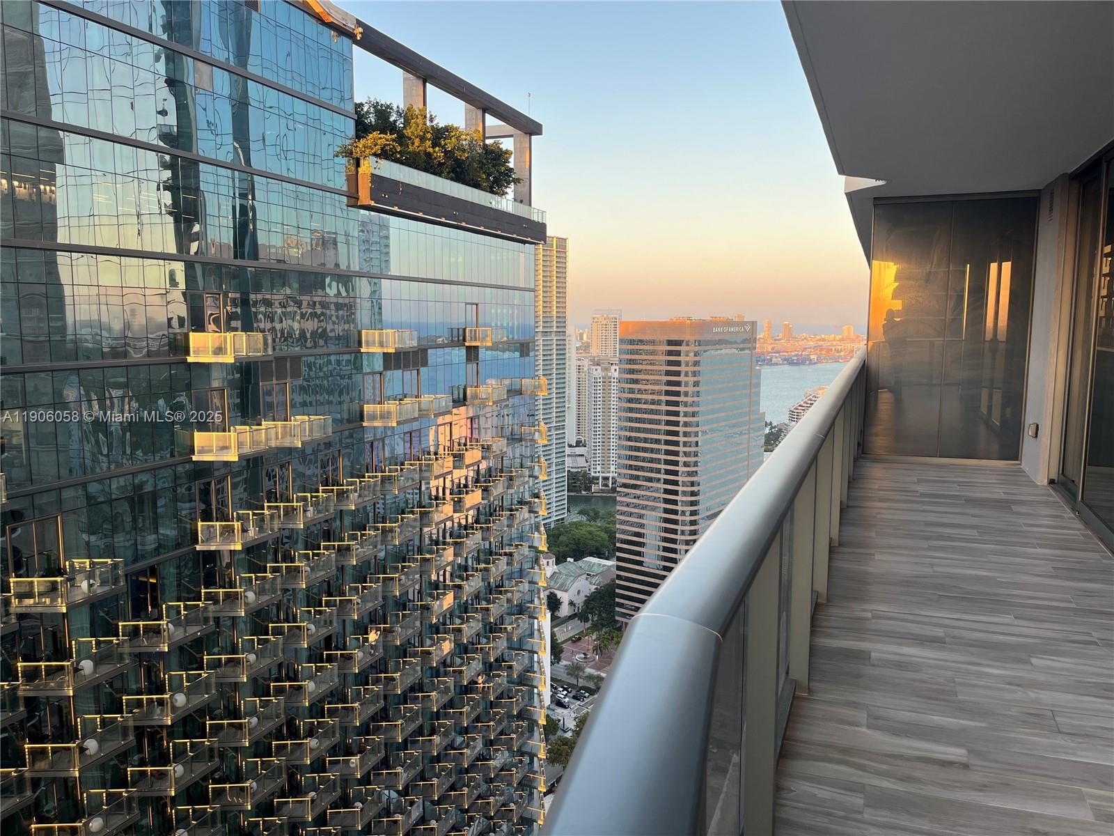 A balcony with wood-look tile flooring overlooks a neighboring glass skyscraper and city skyline — 801 S Miami Ave # 4309, Miami FL 33130, MIAMI, FL