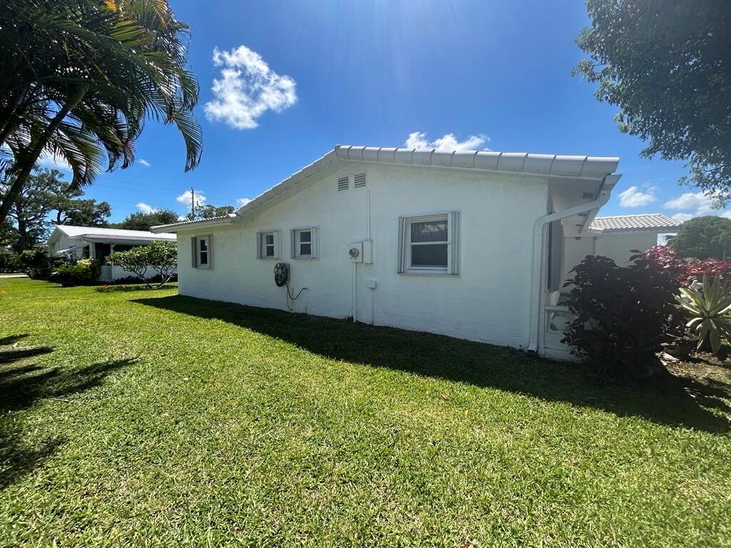 The exterior side of a white, single-story house features a lawn and several windows — 1902 SW 22nd Avenue, Boynton Beach FL 33426, BOYNTON BEACH, FL