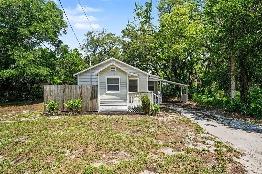 A small, light-colored house with a wooden fence and a carport sits among trees — 828 E 145TH AVENUE, TAMPA, FL