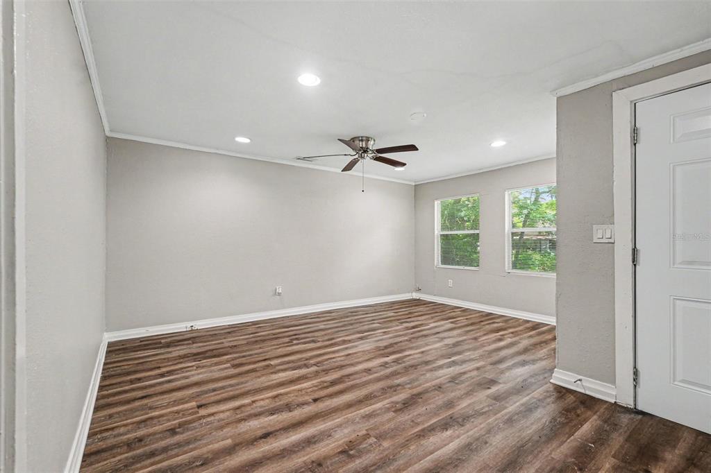 An empty room features light gray walls, wood-look flooring, a ceiling fan, and two windows — 828 E 145TH AVENUE, TAMPA, FL