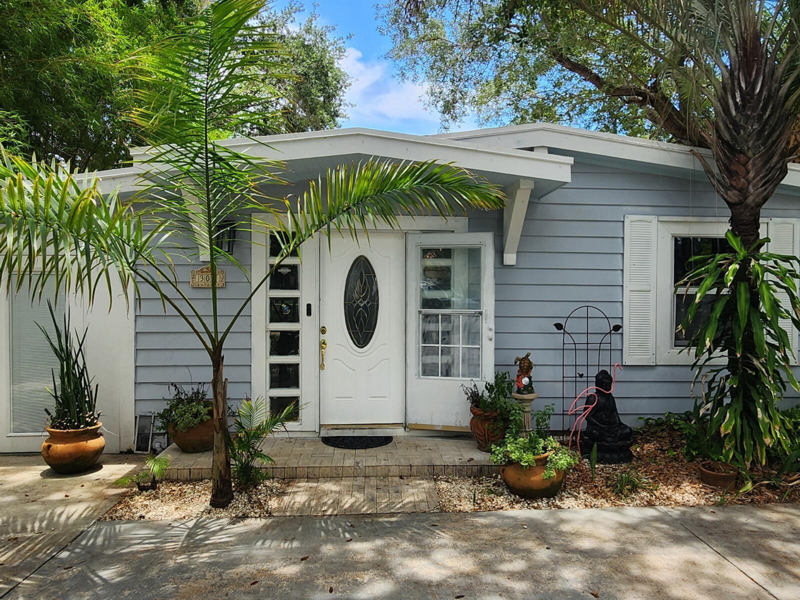 The exterior of a light blue house features a white front door and palm trees — 305 S Loxahatchee Drive, Jupiter FL 33458, JUPITER, FL