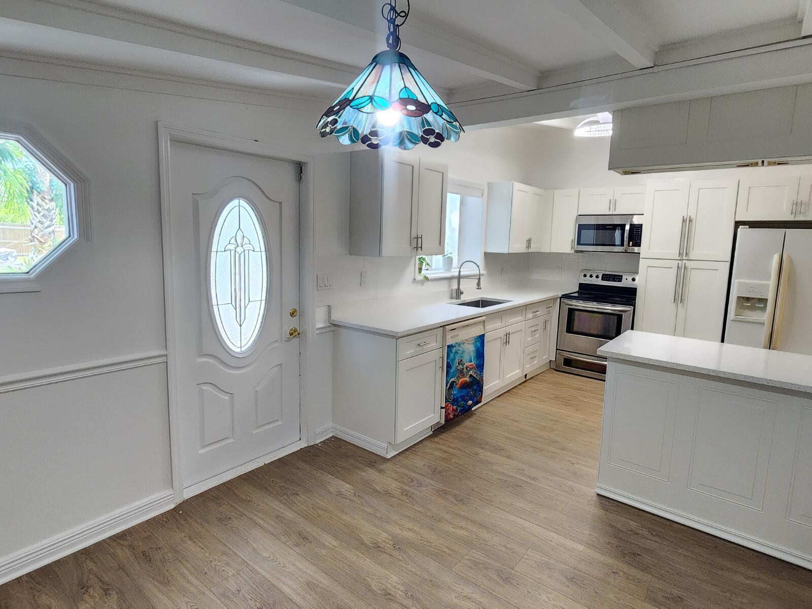A white kitchen features wood-look flooring, stainless steel appliances, and a decorative stained-glass pendant light — 305 S Loxahatchee Drive, Jupiter FL 33458, JUPITER, FL
