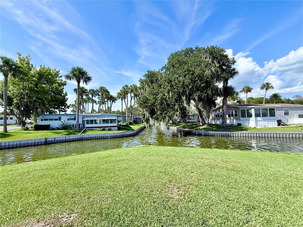 A canal flows between two manufactured homes surrounded by palm trees and large oak trees — 29 CLUB HOUSE, EUSTIS, FL