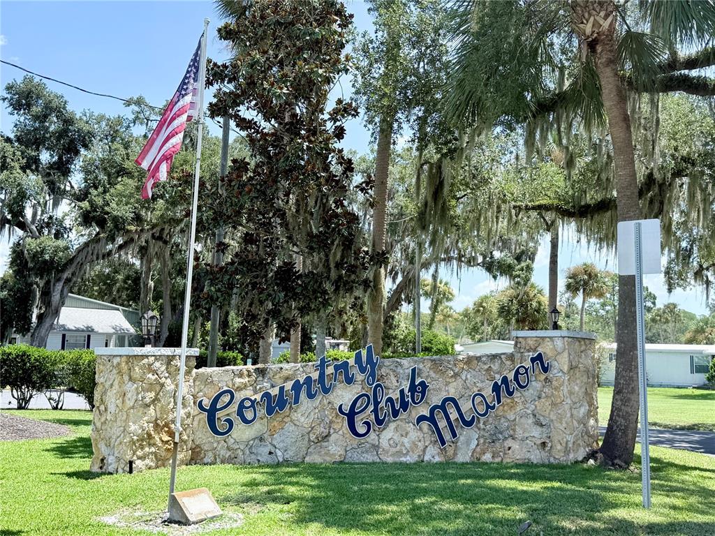 A stone monument sign for Country Club Manor stands on a lawn with an American flag — 29 CLUB HOUSE, EUSTIS, FL