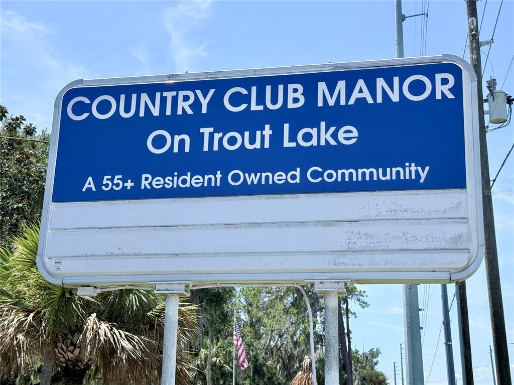 A blue sign for Country Club Manor on Trout Lake stands outdoors — 29 CLUB HOUSE, EUSTIS, FL