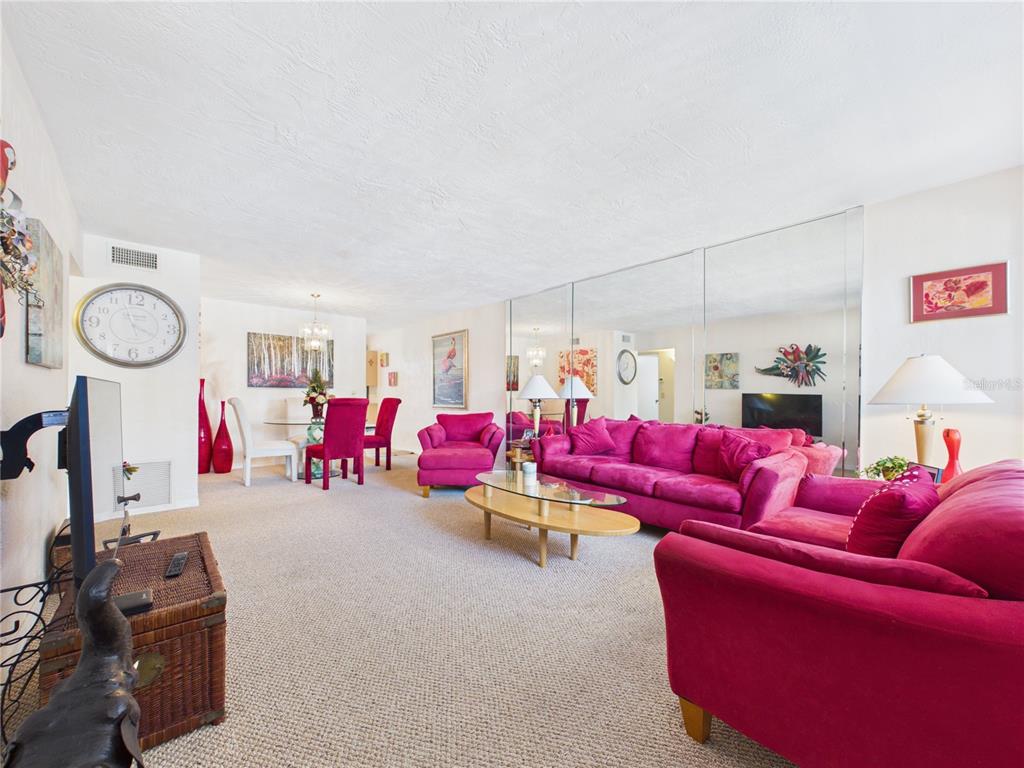 A living and dining room features bright pink furniture, a mirrored wall, and beige carpeting — 2462 BRAZILIA DRIVE UNIT 42, CLEARWATER, FL