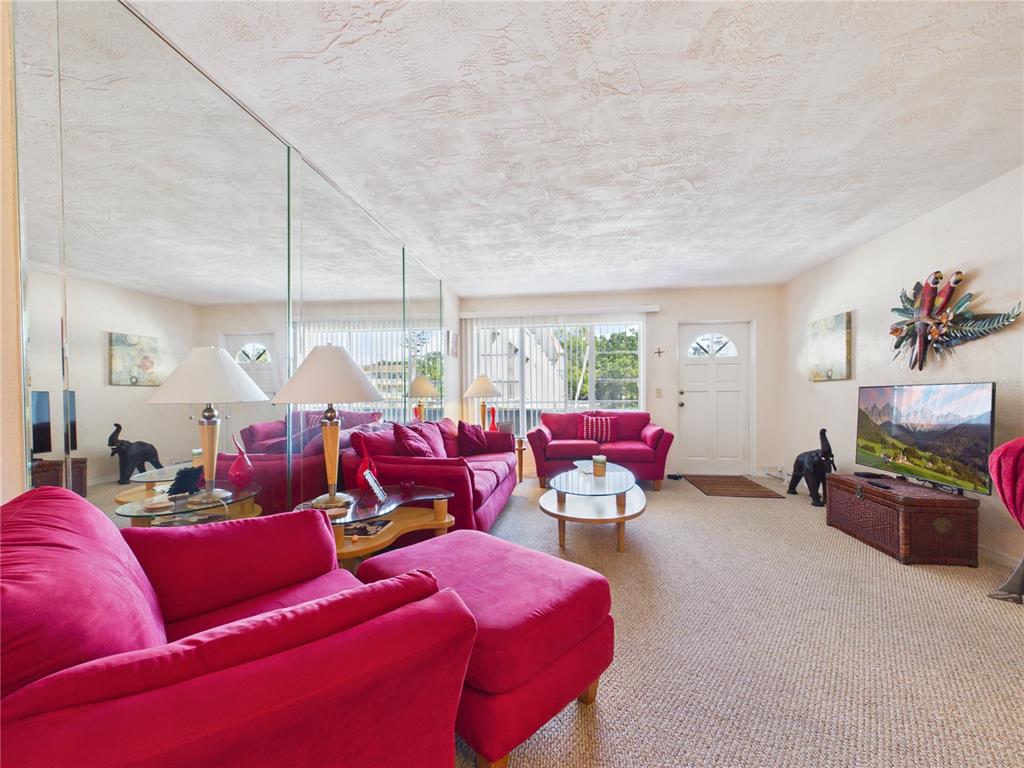 A living room features bright pink sofas, a mirrored wall, and a television on a chest — 2462 BRAZILIA DRIVE UNIT 42, CLEARWATER, FL