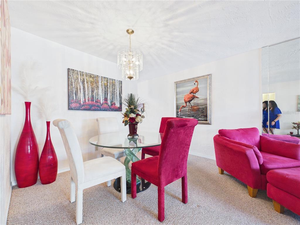A dining area features a glass table, mixed chairs, a chandelier, and pink accent decor — 2462 BRAZILIA DRIVE UNIT 42, CLEARWATER, FL