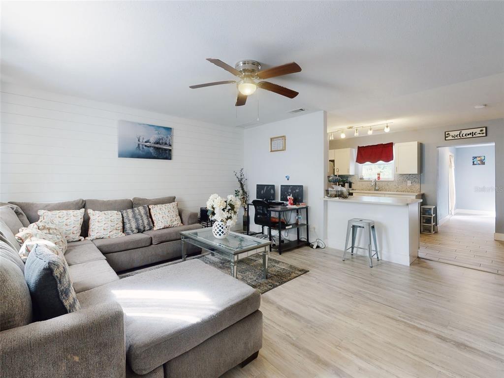 A living room with a sectional sofa, coffee table, desk, and an open kitchen area — 5476 W BAYSHORE DRIVE, PORT ORANGE, FL