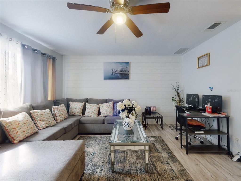 A living room features a gray sectional sofa, a glass coffee table, and a desk — 5476 W BAYSHORE DRIVE, PORT ORANGE, FL