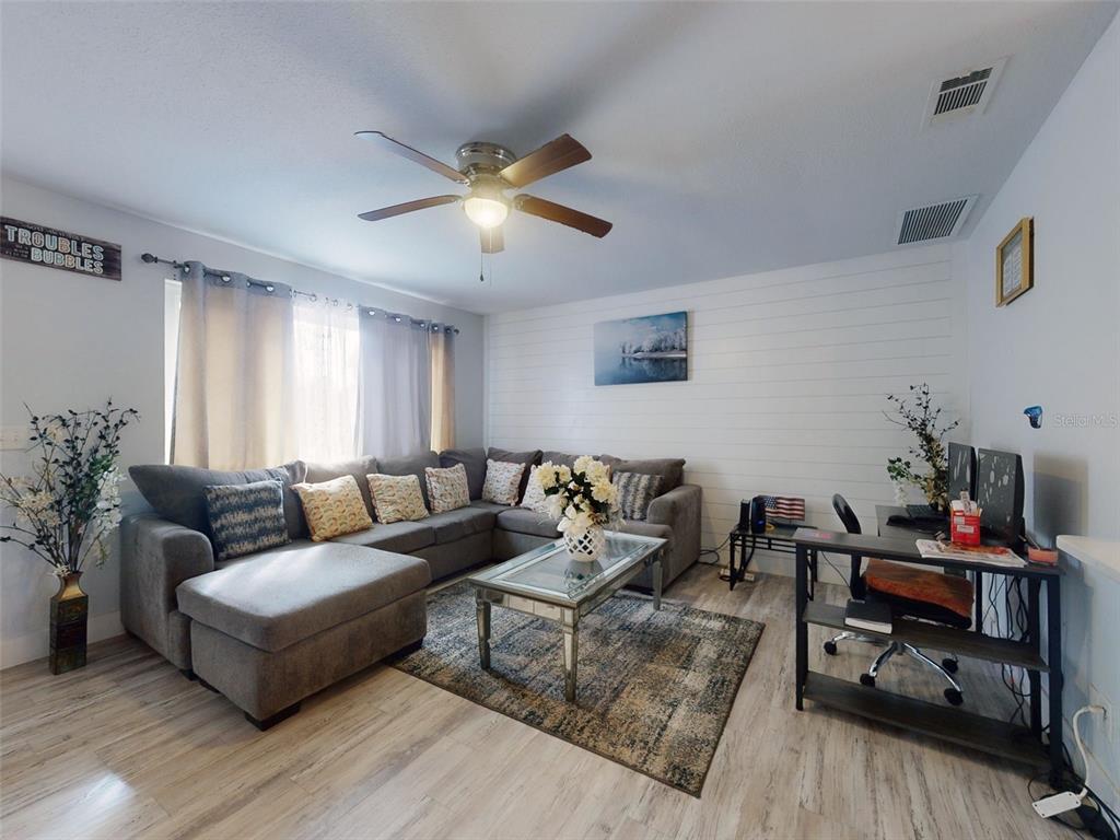 A living room features a gray sectional sofa, a glass coffee table, and a desk area — 5476 W BAYSHORE DRIVE, PORT ORANGE, FL