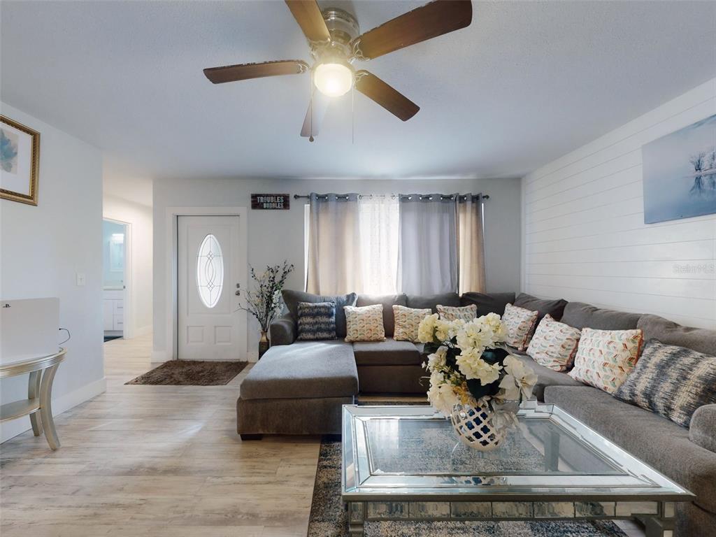 A living room features a gray sectional sofa, a glass coffee table, and wood-look flooring — 5476 W BAYSHORE DRIVE, PORT ORANGE, FL