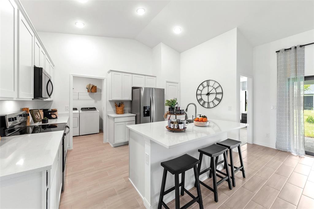 A modern white kitchen features a center island with bar stools and an adjacent laundry room — 3445 W DITTANY DRIVE, CITRUS SPRINGS, FL