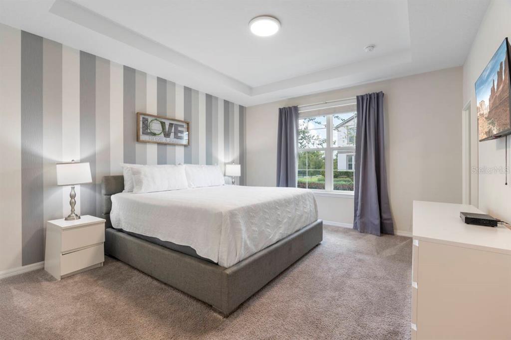 A bedroom features a gray upholstered bed, striped accent wall, and a white dresser — 9029 SUNSHINE RIDGE LOOP, KISSIMMEE, FL