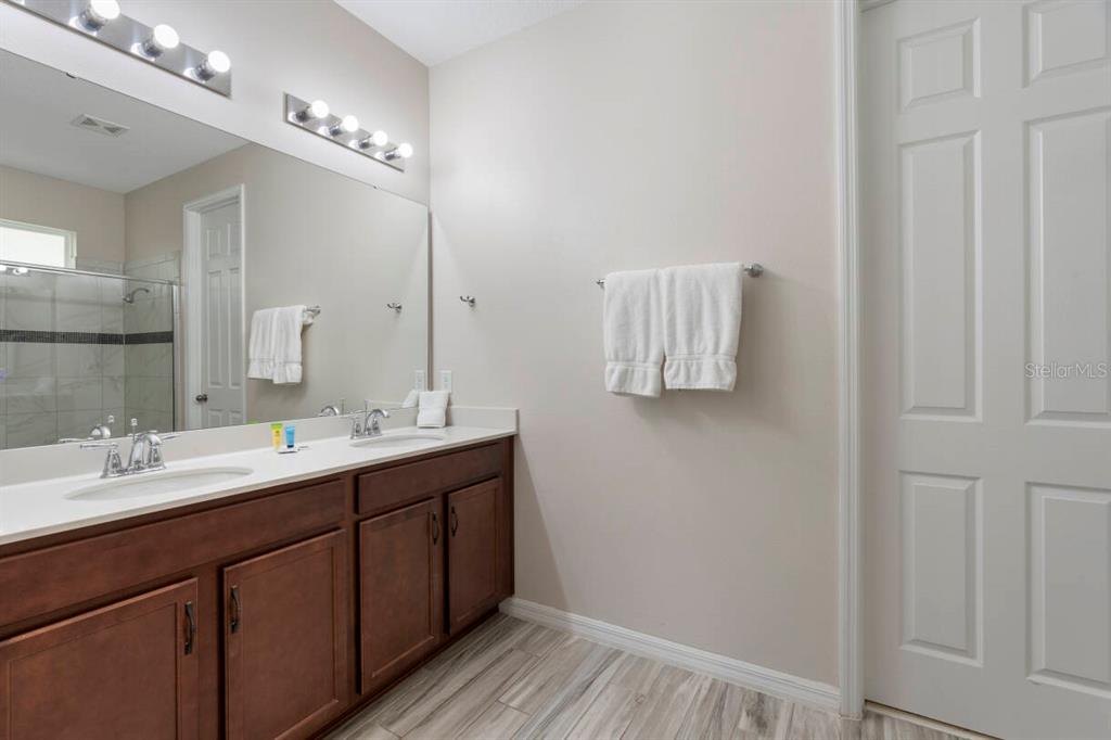 A bathroom features a double-sink vanity with dark wood cabinets and a large wall mirror — 9029 SUNSHINE RIDGE LOOP, KISSIMMEE, FL