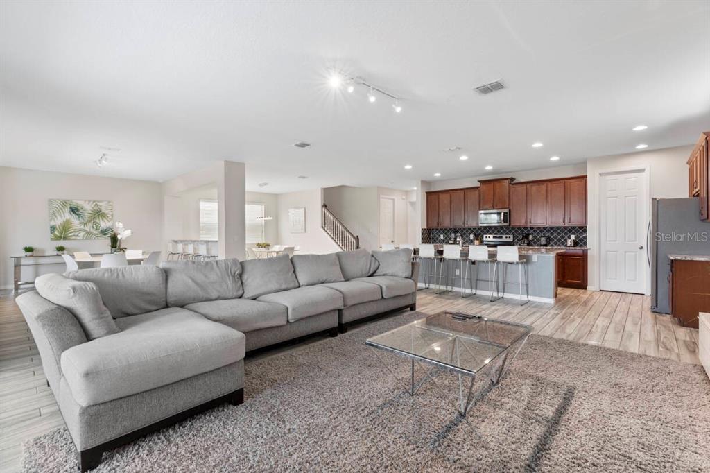 A spacious open-concept living room features a large gray sectional sofa and a modern kitchen — 9029 SUNSHINE RIDGE LOOP, KISSIMMEE, FL