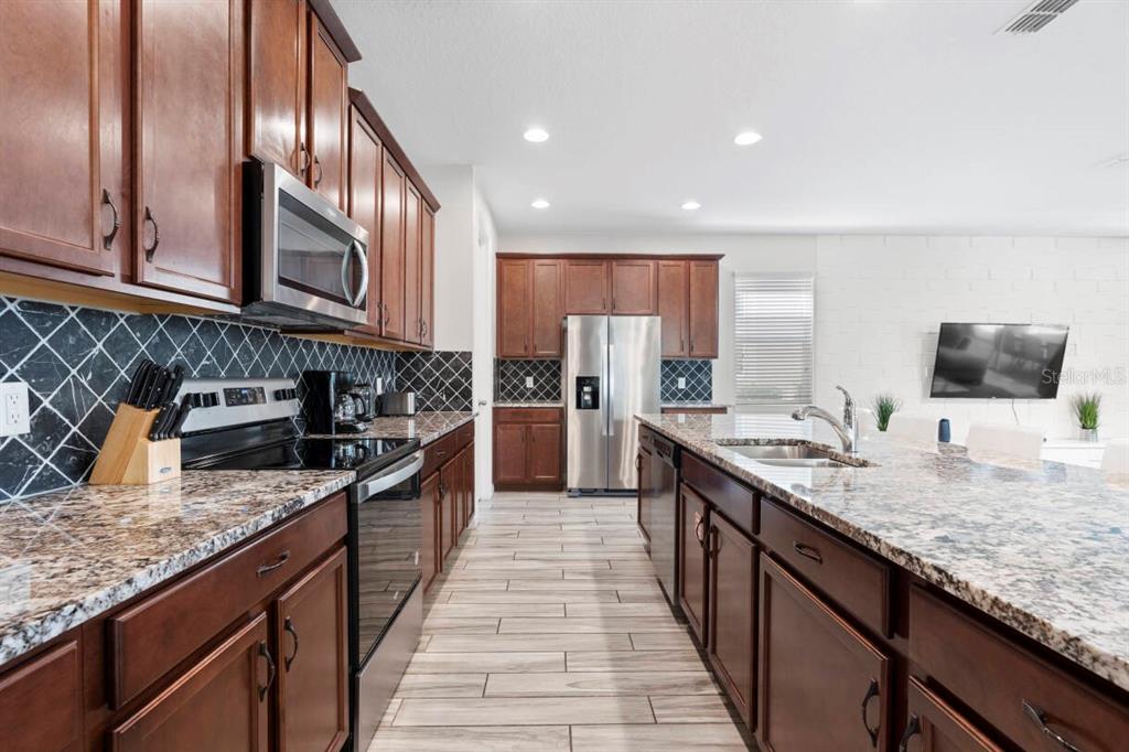 A kitchen features dark wood cabinets, granite countertops, stainless steel appliances, and a tiled floor — 9029 SUNSHINE RIDGE LOOP, KISSIMMEE, FL