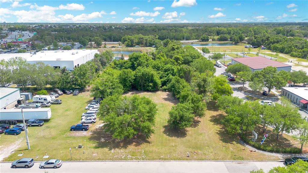 An aerial view shows a vacant, grassy lot surrounded by trees and commercial buildings — 0 LIONS COURT, KISSIMMEE, FL