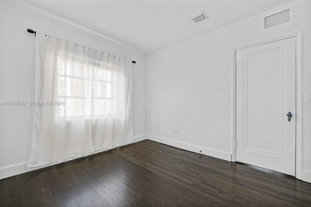 An empty room features white walls, dark hardwood floors, a window with curtains, and a door — 846 Jefferson Ave # 8, Miami Beach FL 33139, MIAMI BEACH, FL
