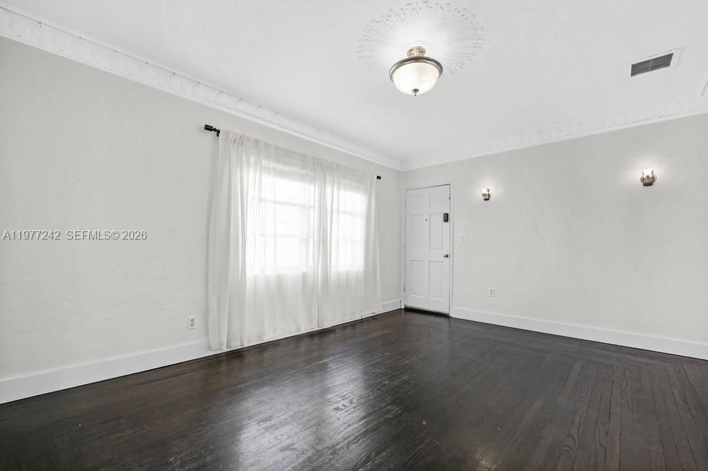An empty room features dark hardwood floors, white walls, a window with curtains, and crown molding — 846 Jefferson Ave # 8, Miami Beach FL 33139, MIAMI BEACH, FL