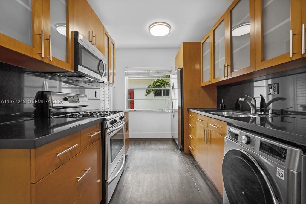 A galley kitchen features wood cabinets, black countertops, stainless steel appliances, and a laundry unit — 846 Jefferson Ave # 8, Miami Beach FL 33139, MIAMI BEACH, FL