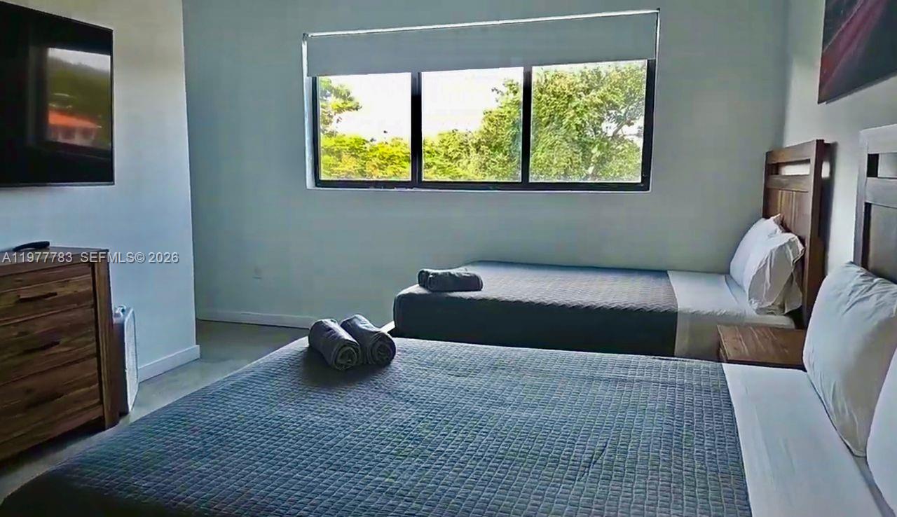 A bedroom features two beds with gray quilts, a wooden dresser, and a large window — 7105 NE 4 Ct, Miami FL 33138, MIAMI, FL