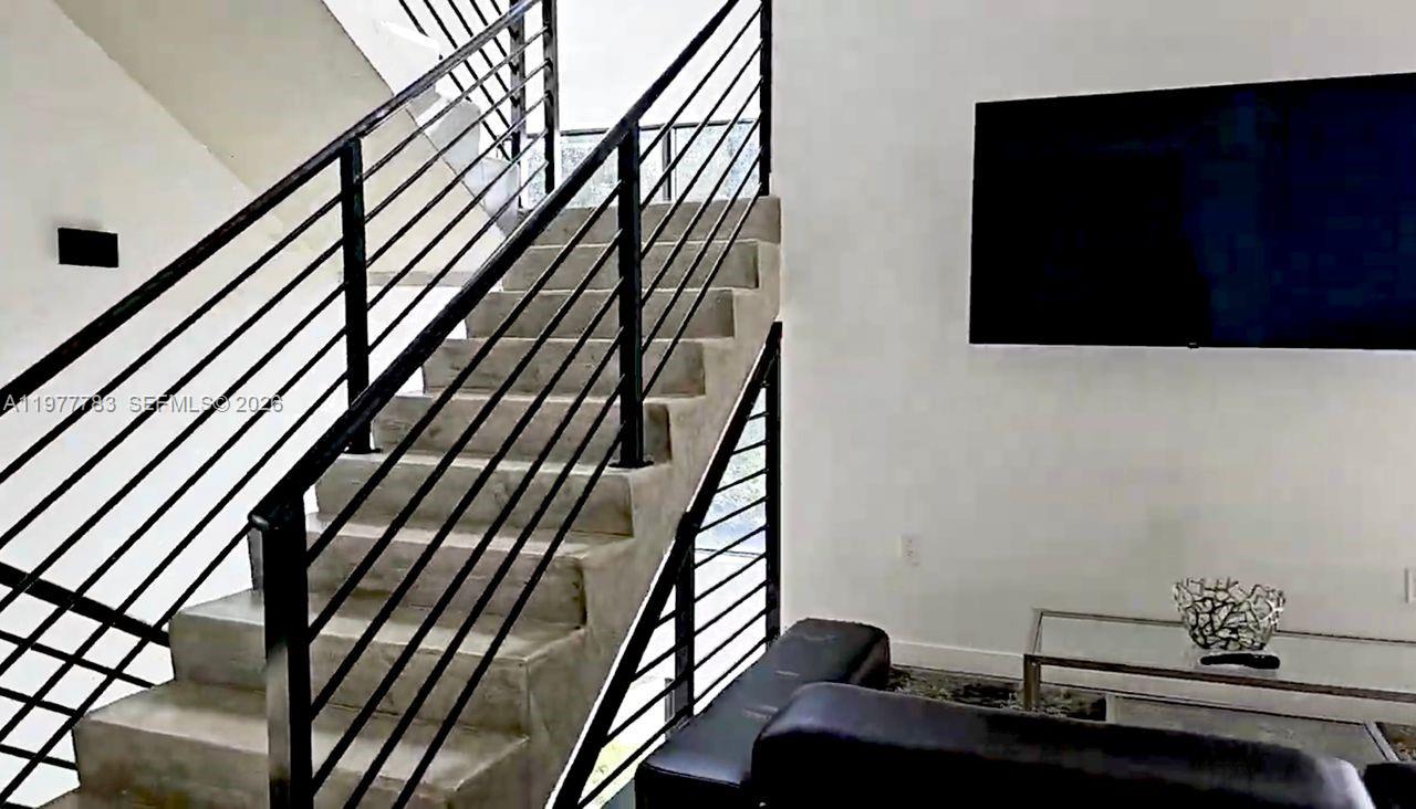 A staircase with black metal railings leads upward in a room with a television — 7105 NE 4 Ct, Miami FL 33138, MIAMI, FL