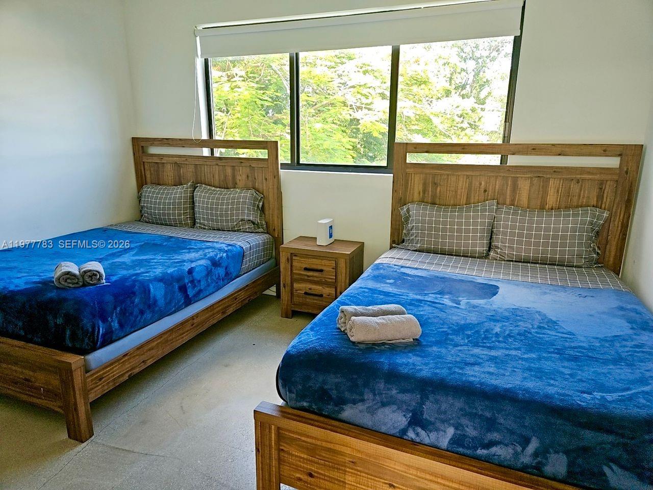 A bedroom features two wooden bed frames with blue blankets and a central nightstand — 7105 NE 4 Ct, Miami FL 33138, MIAMI, FL