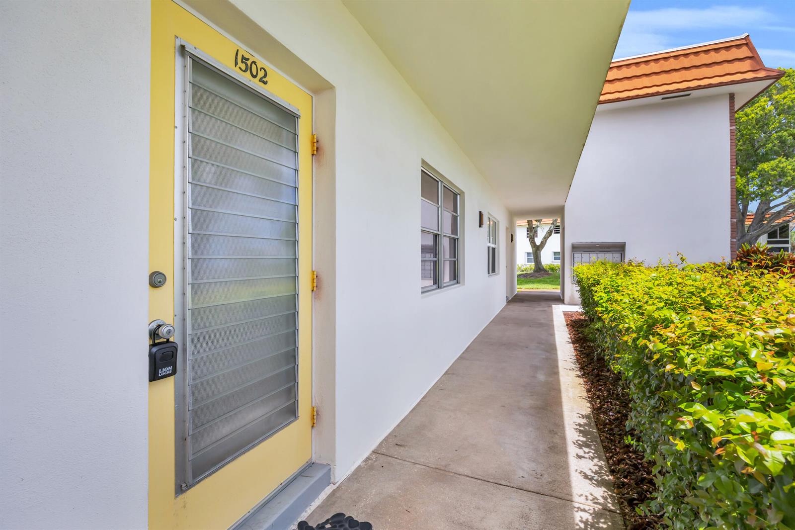 A yellow front door with a louvered glass insert sits along a concrete walkway — 1225 NW 21st Street # 1502, Stuart FL 34994, STUART, FL