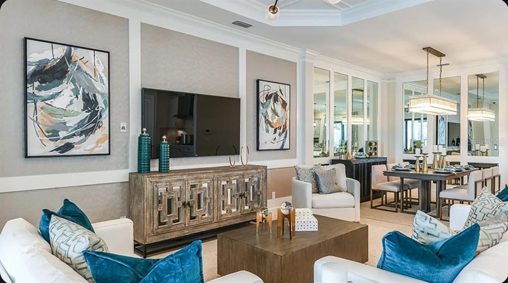 A living room features a wall-mounted television, mirrored console, and blue accent pillows on sofas — 3114 VICENZA COURT, BRADENTON, FL