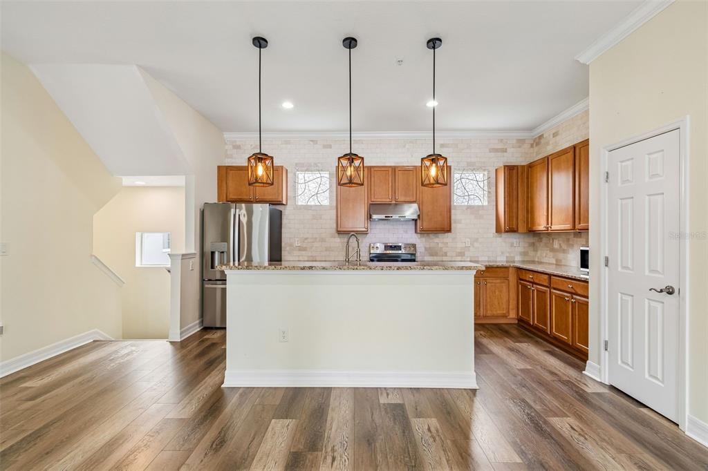 A kitchen features wood cabinets, a granite-topped island, stainless steel appliances, and wood-look flooring — 4516 BAY SPRING COURT, TAMPA, FL