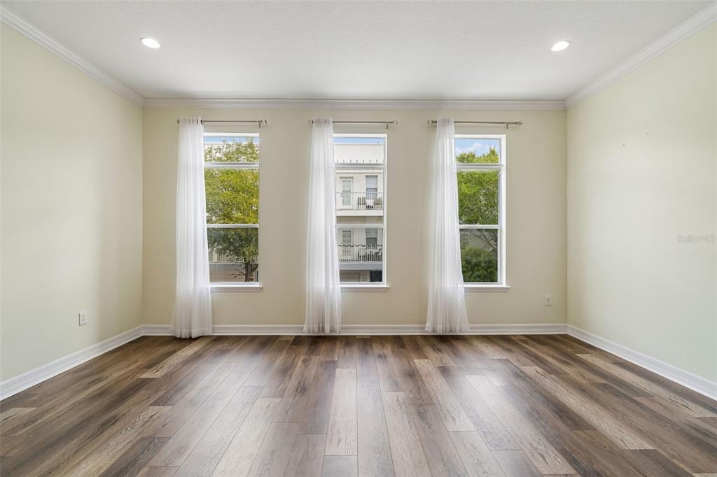 An empty room features wood-look flooring, light-colored walls, and three windows with white curtains — 4516 BAY SPRING COURT, TAMPA, FL