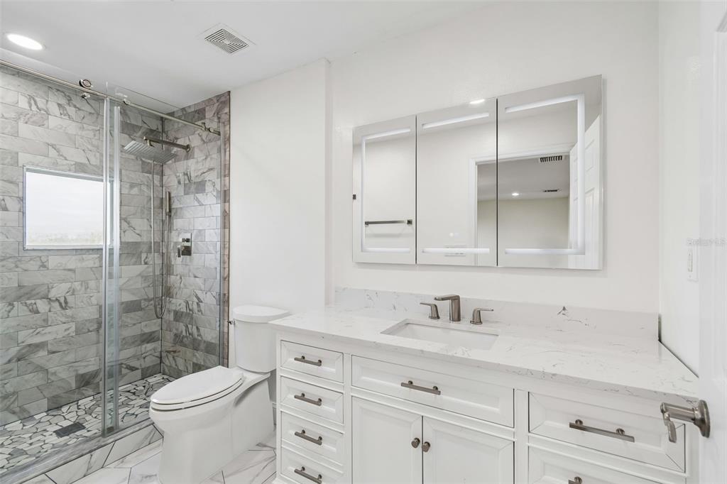 A bathroom features a white vanity, a marble-tiled walk-in shower, and a lighted medicine cabinet — 4516 BAY SPRING COURT, TAMPA, FL