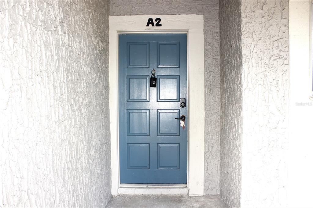 A blue front door labeled A2 is set within a textured gray stucco exterior wall — 6336 NEWTOWN CIRCLE UNIT 36A2, TAMPA, FL
