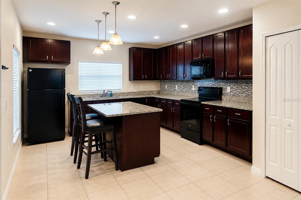 A kitchen features dark wood cabinets, granite countertops, black appliances, and a central island — 233 PRIMROSE DRIVE, DAVENPORT, FL