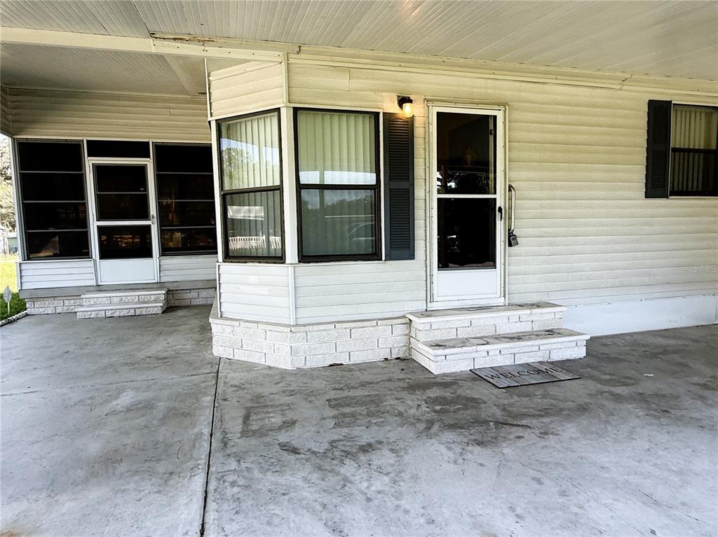 A concrete carport leads to a white mobile home with a bay window and steps — 4550 CHARTER STREET, ZEPHYRHILLS, FL
