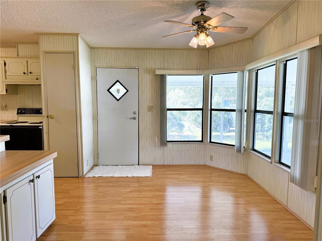 A dining area with light wood flooring, vertical paneling, a ceiling fan, and large windows — 4550 CHARTER STREET, ZEPHYRHILLS, FL