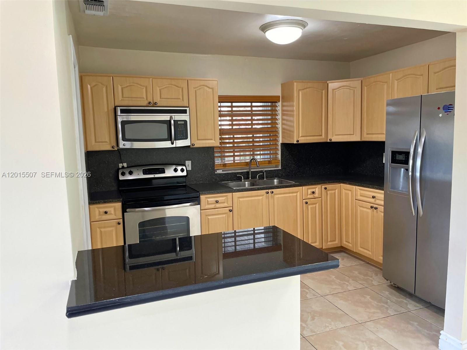 A kitchen features light wood cabinets, black countertops, stainless steel appliances, and tile flooring — 22430 SW 113th Ct, Miami FL 33170, MIAMI, FL