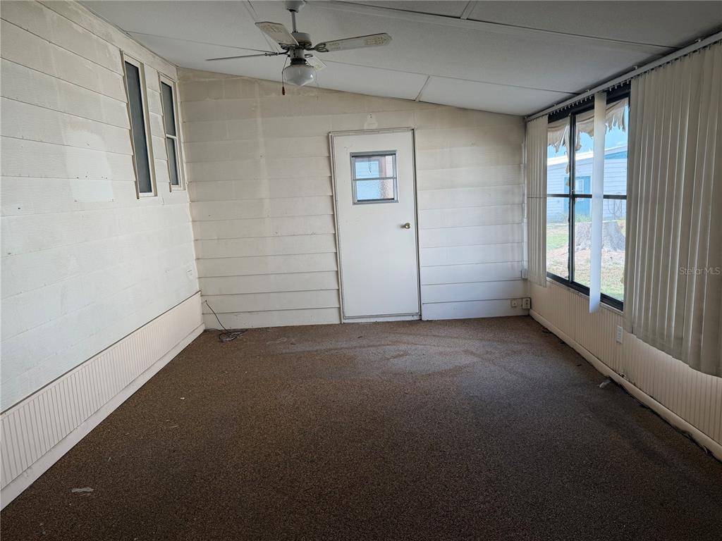 An enclosed porch features brown carpeting, wood-paneled walls, a ceiling fan, and stairs leading indoors — 1007 CASSANDRA LANE, LAKELAND, FL