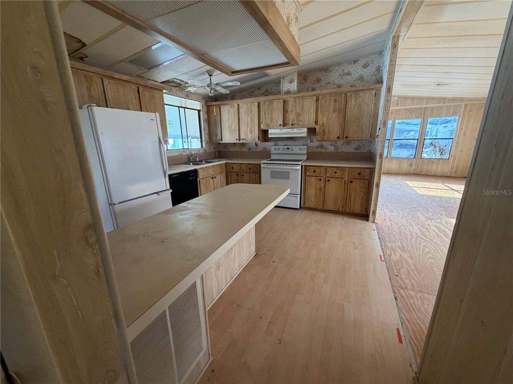 A kitchen with wood cabinets and a breakfast bar overlooks a room with water damage — 1007 CASSANDRA LANE, LAKELAND, FL