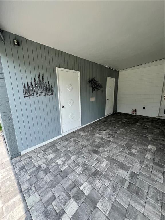 A covered patio features gray vertical siding, two white doors, and gray paver flooring — 1950 Cortez Boulevard, Fort Pierce FL 34982, FORT PIERCE, FL