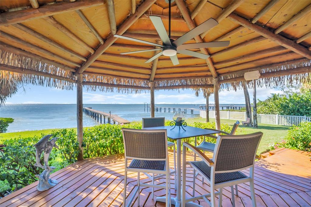 A wooden gazebo with a ceiling fan overlooks a grassy lawn, a pier, and water — 1100 FRIENDLY WAY S, ST PETERSBURG, FL