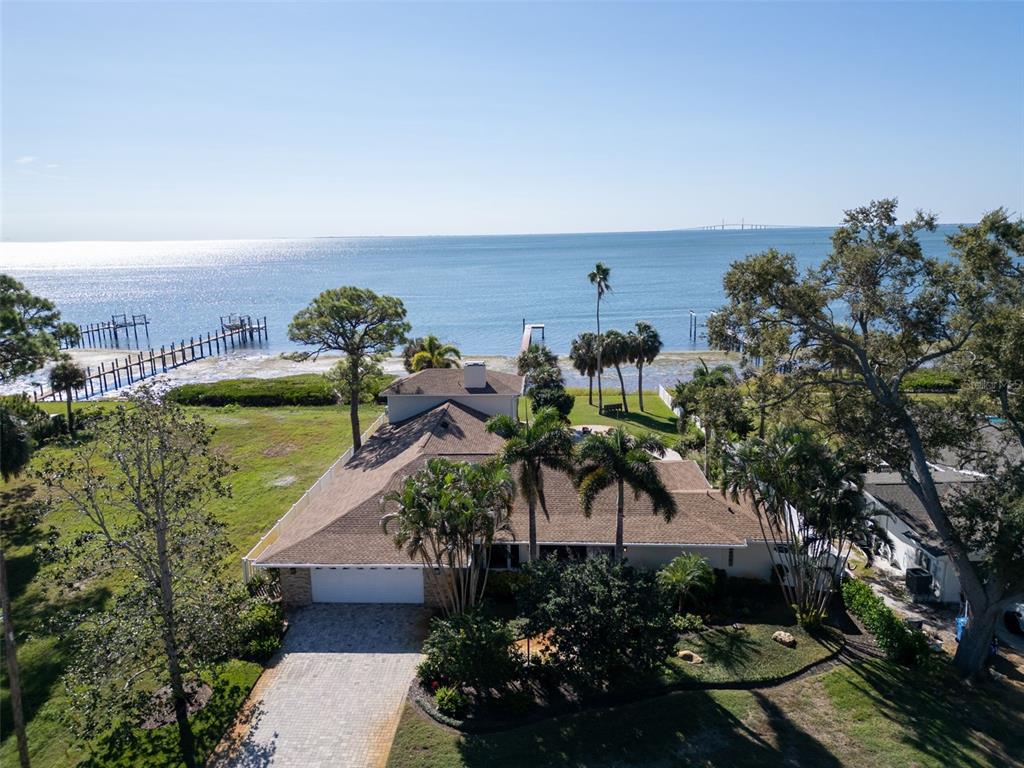 An aerial view shows a waterfront house with a paved driveway, palm trees, and dock — 1100 FRIENDLY WAY S, ST PETERSBURG, FL
